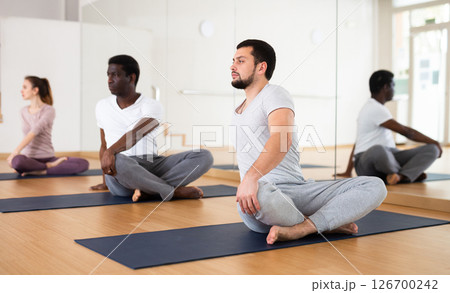 Man practising lotus pose with group in gym 126700242