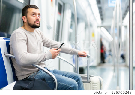 Bearded traveler sitting with suitcase and smartphone in metro car Bearded traveler sitting with suitcase and smartphone in metro car 126700245