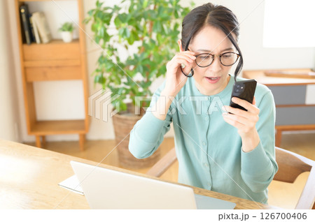 スマホを片手にパソコンを見ながら悩み中のミドル女性 126700406