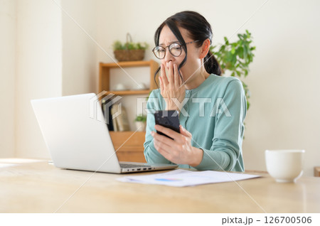 スマホを片手にパソコンを見ながら驚くミドル女性 126700506
