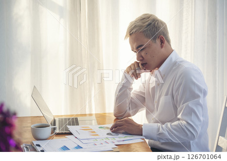 Asian Businessman using laptop calling phone at office desk. Man wear eye glasses talking smartphone read financial graph chart Planning marketing info. Happy Asian business people work office firm 126701064