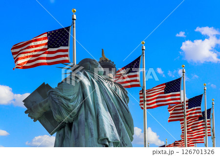 Statue of Liberty stands proudly with multiple American flags fluttering in Ney York US 126701326