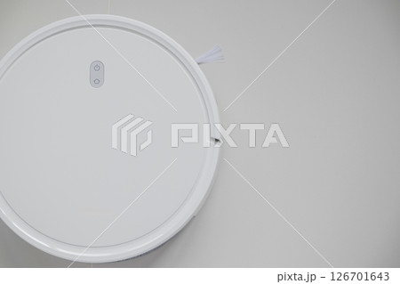 White automatic floor cleaner with side brush on tile flooring. Top view of robot vacuum cleaner removing dust, showcasing modern smart home cleaning technology for spotless and efficient maintenance White automatic floor cleaner with side brush on tile flooring. Top view of robot vacuum cleaner removing dust, showcasing modern smart home cleaning technology for spotless and efficient maintenance 126701643