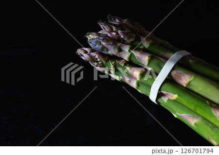 Raw asparagus on black background. Green and violet asparagus on dark stone surface. Springtime vitamins. Healthy eating. Farm to table concept. Asparagus bundle isolated. Raw asparagus on black background. Green and violet asparagus on dark stone surface. Springtime vitamins. Healthy eating. Farm to table concept. Asparagus bundle isolated. 126701794