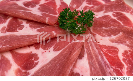 Thinly sliced raw pork arranged in a floral pattern with fresh parsley garnish. suitable for food menus, hotpot restaurants, or culinary advertising. 126702087