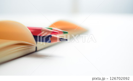 Close-up of colored pencils placed inside the fold of an open notebook, with shallow depth of field and soft light. Represents creativity, inspiration, and back-to-school themes. Close-up of colored pencils placed inside the fold of an open notebook, with shallow depth of field and soft light. Represents creativity, inspiration, and back-to-school themes. 126702092
