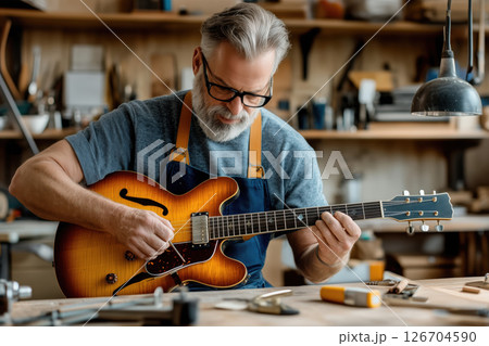 Man restoring an old guitar by sanding in a woodworking workshop 126704590