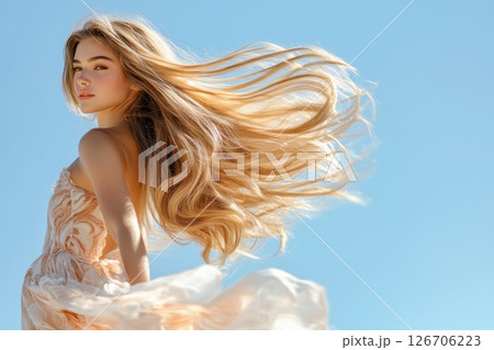 Young woman with long flowing blond hair radiates grace against a pale blue sky in sunlight 126706223