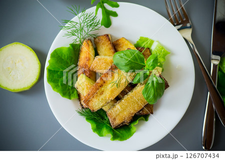Fried zucchini slices with salad greens on a gray background Fried zucchini slices with salad greens on a gray background 126707434