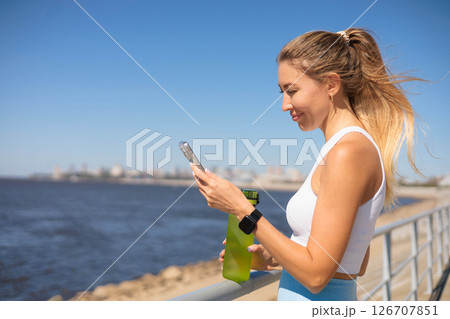 Active sport woman with water bottle use smartphone at river embankment closeup 126707851