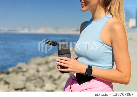 Smiling young blonde woman jogger runner drink water from bottle at river embankment closeup 126707867