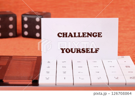 Believe in yourself, overcoming challenges concept. CHALLENGE YOURSELF text on a business card with game cubes in the background and a calculator in the foreground Believe in yourself, overcoming challenges concept. CHALLENGE YOURSELF text on a business card with game cubes in the background and a calculator in the foreground 126708864