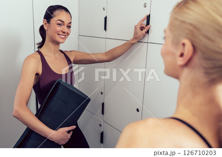 Two young women in the gym talking in the locker room 126710203
