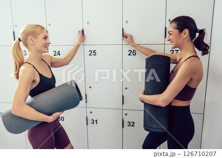 Two young women with rolled mats in near lockers in the gym 126710207