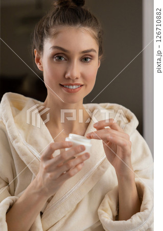 Trendy woman in robe practices personal facial care using gentle cleanser and cosmetics Trendy woman in robe practices personal facial care using gentle cleanser and cosmetics 126710882