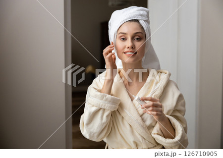Woman with towel wrapped around her head gently applying cream into her skin Woman with towel wrapped around her head gently applying cream into her skin 126710905