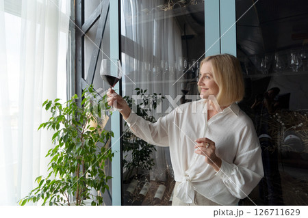 An Elegant Woman Joyfully Toasting with a Glass of Rich Red Wine in a Beautifully Stylish Kitchen Space 126711629