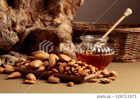 Almond nuts in a wooden dish and honey in a glass jar. Almond nuts in a wooden dish and honey in a glass jar. 126711973