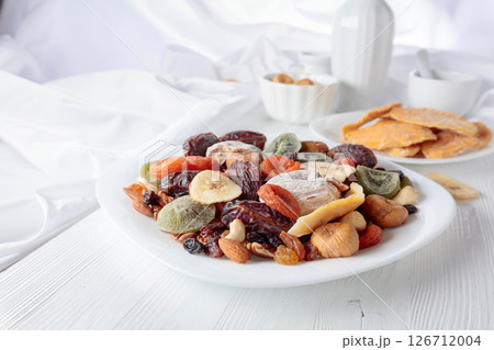 Mix of dried tropical fruits, nuts, and raisins on a white table. Mix of dried tropical fruits, nuts, and raisins on a white table. 126712004