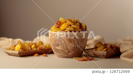 Yellow sultana raisins in a wooden bowl on a beige background. 126712009
