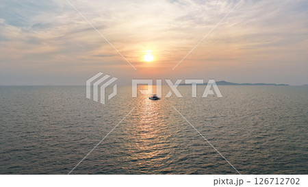 Catamaran sailing towards sunset over calm ocean with island in background Catamaran sailing towards sunset over calm ocean with island in background 126712702