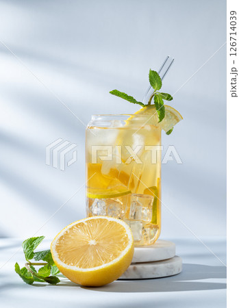 Iced drink with lemon and mint in a glass on a marble stand on light background with sunlight Iced drink with lemon and mint in a glass on a marble stand on light background with sunlight 126714039