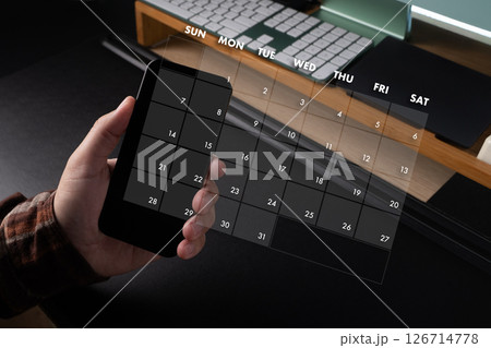 2025 calendar person holding smartphone with digital calendar overlay showing days of week and dates, workspace with keyboard and desk organizer 126714778