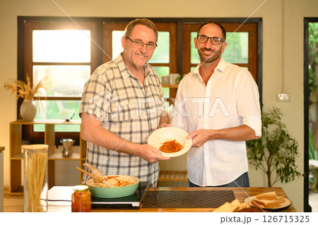 Elderly father and adult son presenting their finished meal in a warm home kitchen. Fathers day concept Elderly father and adult son presenting their finished meal in a warm home kitchen. Fathers day concept 126715325