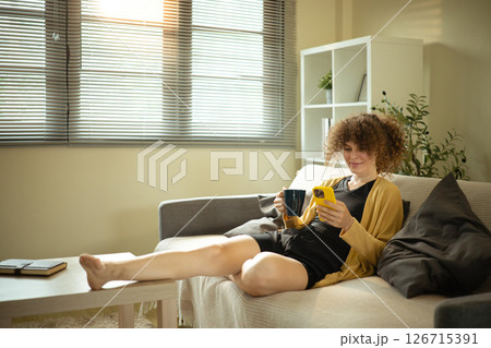 Young woman with curly hair lounging on the sofa and using her smartphone Young woman with curly hair lounging on the sofa and using her smartphone 126715391