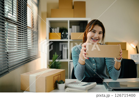 Smiling female entrepreneur holding a package preparing a product for shipment Smiling female entrepreneur holding a package preparing a product for shipment 126715400