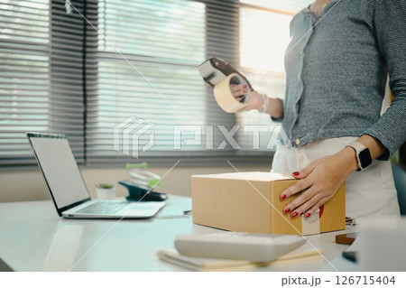 Young small business owner packing products for shipping in her home office Young small business owner packing products for shipping in her home office 126715404
