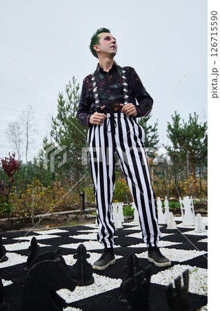 A Stylish Individual Wearing Striped Pants Poses at an Outdoor Chess Board Under the Sun 126715590