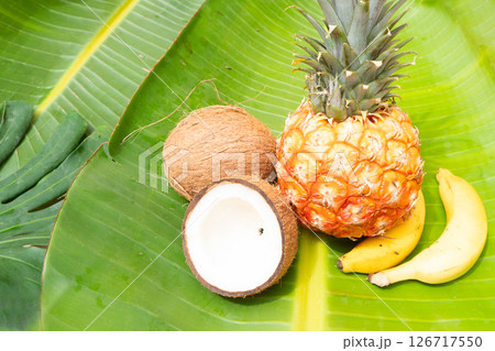 A Fresh Pineapple adorned with a Tropical Flower resting on vibrant Green Leaves, capturing the essence of paradise 126717550