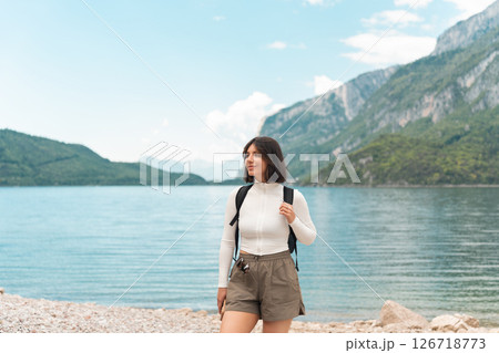 Lost in the moment, a happy woman hikes a quiet path between green hills, the lake glinting nearby and the mountains rising like a dream 126718773