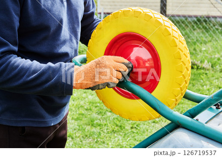 Focusing on mounting process, builder secures flat free wheel to utility cart to enhance stability and extend lifespan of essential equipment. 126719537