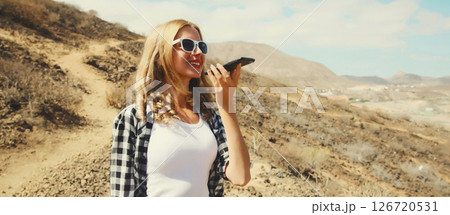 Happy young woman holding smartphone using takes calling on a hiking trail on top of the mountain Happy young woman holding smartphone using takes calling on a hiking trail on top of the mountain 126720531
