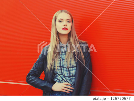 Fashion portrait of beautiful blonde young woman posing in black leather jacket on red background 126720677