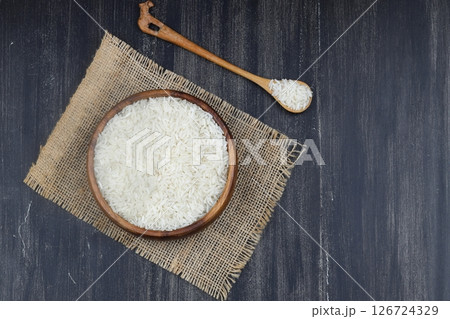 Raw white rice on wooden background. Long uncooked rice in wooden plate. Natural organic food. Traditional Asian cereal culture. Raw white rice on wooden background. Long uncooked rice in wooden plate. Natural organic food. Traditional Asian cereal culture. 126724329