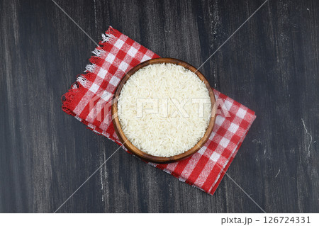 Raw white rice on wooden background. Long uncooked rice in wooden plate. Natural organic food. Traditional Asian cereal culture. 126724331