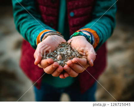 Child holding soil and small sprout in hands while standing outdoors 126725045