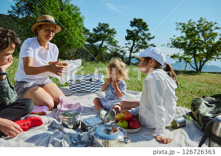 Family Enjoying a Relaxing Picnic in Scenic Mountain Landscape on a Warm, Sunny Day Family Enjoying a Relaxing Picnic in Scenic Mountain Landscape on a Warm, Sunny Day 126726363