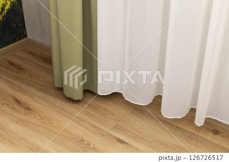 Light filters through sheer curtains, highlighting a cozy indoor setting with wooden flooring and a touch of greenery on the wall, creating a peaceful atmosphere Light filters through sheer curtains, highlighting a cozy indoor setting with wooden flooring and a touch of greenery on the wall, creating a peaceful atmosphere 126726517