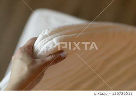 A hand holds a zippered bedding cover made of soft material, showcasing its design and functionality in a cozy indoor environment. Perfect for enhancing sleep quality A hand holds a zippered bedding cover made of soft material, showcasing its design and functionality in a cozy indoor environment. Perfect for enhancing sleep quality 126726518