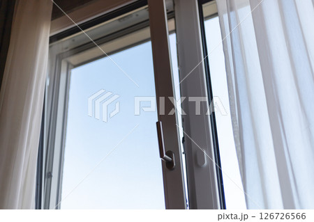 Soft sunlight filters into a room through an open window adorned with sheer curtains. The clear blue sky provides a bright, inviting atmosphere, suggesting a peaceful morning 126726566