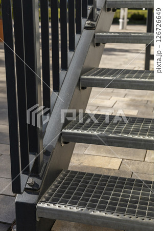 Sturdy metal stairs provide access to raised platform situated in sunny outdoor garden. The steps feature a functional design with a grid pattern for safety. Metal construction, welding, steel stairs. 126726649