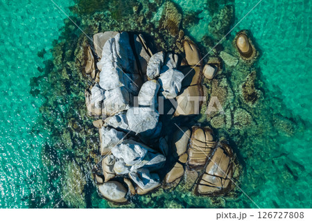 Rugged coastal rock formation emerging from clear turquoise waters in a serene seaside location Rugged coastal rock formation emerging from clear turquoise waters in a serene seaside location 126727808