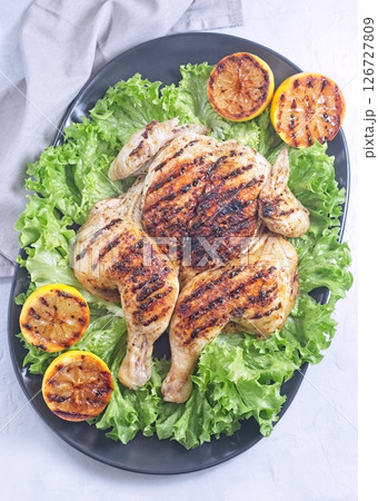 Spatchcocked grilled chicken with lemon garlic marinade on lettuce with lemon, vertical top view Spatchcocked grilled chicken with lemon garlic marinade on lettuce with lemon, vertical top view 126727809