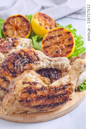 Grilled chicken legs and breast with lemon and lettuce on wooden board, vertical 126727812