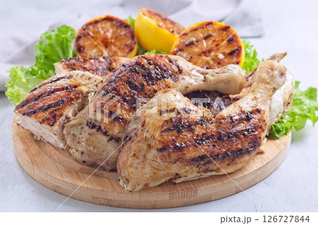 Grilled chicken legs and breast with lemon and lettuce on wooden board, horizontal Grilled chicken legs and breast with lemon and lettuce on wooden board, horizontal 126727844