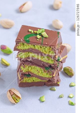 Stack of pistachio Dubai style chocolate bars with whole pistachios showing filling, vertical 126727846